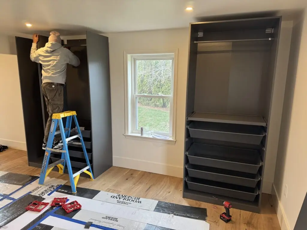 Assemblix installer on a ladder fitting a gray closet system into a bedroom nook
