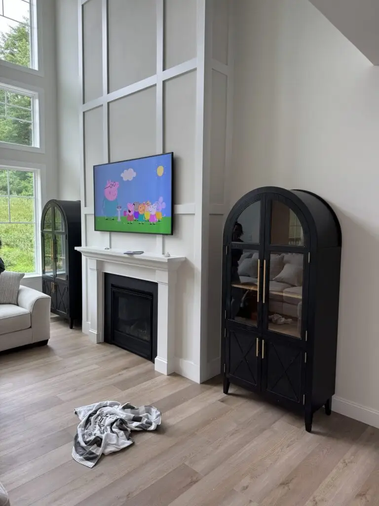 TV mounted above a white fireplace beside an arched black display cabinet